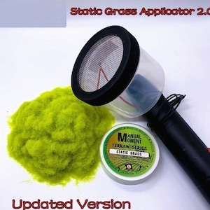 Op de afbeelding: Een statische grasaanbrenger 2.0 met een zwarte handgreep en een doorzichtige container. Een hoop felgroen statisch gras en een container met statisch gras zijn ook aanwezig. De tekst "Static Grass Applicator 2.0" en "Updated Version" zijn zichtbaar.