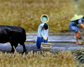 Könnte beinhalten: Eine schwarze Kuhfigur mit weißen Markierungen im Gesicht steht auf einem Feld aus braunem Gras. Zwei Miniaturfiguren sind im Hintergrund zu sehen, eine trägt einen Eimer und die andere einen Strohhut.