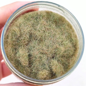 Może przedstawiać: Zbliżenie na słoik wypełniony zielonymi i brązowymi włóknami statycznej trawy. Włókna są długie i puszyste, tworząc realistyczną teksturę trawy.