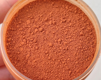 May include: A close-up view of a jar filled with a fine, orange-brown powder. The powder has a slightly grainy texture and appears to be evenly distributed throughout the jar.