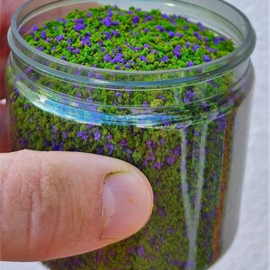 以下が含まれることがあります： 緑と紫のフロッキングが詰まった透明なプラスチック製の瓶。模型鉄道やその他のクラフトに使用されるクラフト素材の一種です。