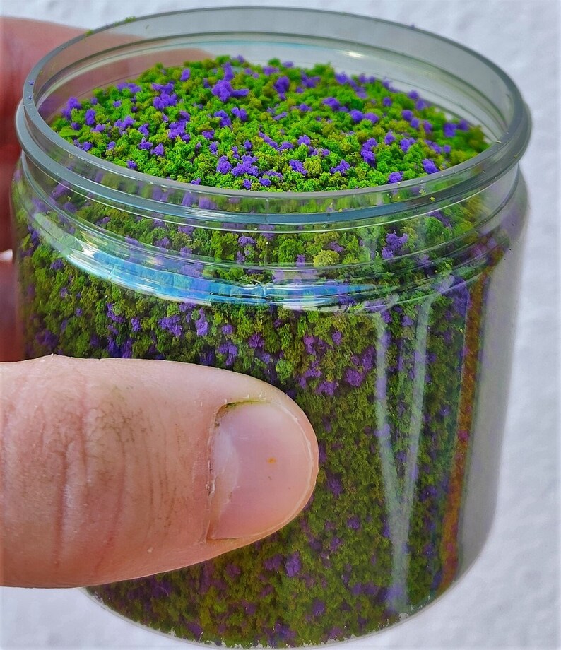 以下が含まれることがあります： 緑と紫のフロッキングが詰まった透明なプラスチック製の瓶。模型鉄道やその他のクラフトに使用されるクラフト素材の一種です。