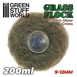 Może przedstawiać: Pojemnik o pojemności 200 ml z brązowym mchem trawiastym, o długości 9-12 mm. Mech jest pokazany obok monety euro w celu porównania rozmiarów. Pojemnik jest oznaczony etykietą "Green Stuff World Grass Flock Brown Moor Grass".