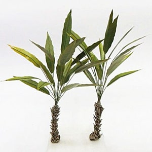 May include: Two artificial green palm trees with brown textured trunks. The trees are on a white background.