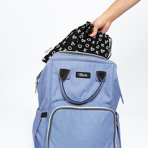 Op de afbeelding: Een lichtblauwe luiertas met een zwarte rits en een zwarte handgreep. De tas heeft een groot voorvak met een rits. De tas wordt gevuld met een zwarte trekkoordtas met een wit "XOXO"-patroon.