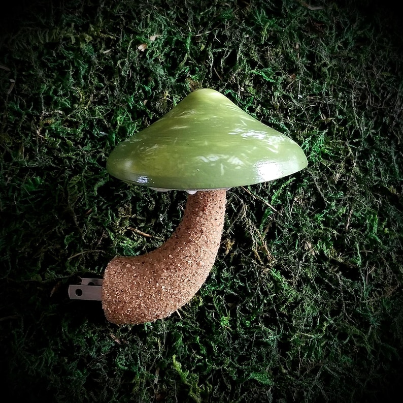 Pode incluir: Uma luz noturna de cer&acirc;mica verde em forma de cogumelo com uma base texturizada marrom e um plugue.