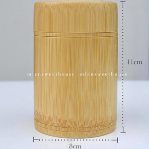 Może przedstawiać: Cylindryczny pojemnik z bambusa z pokrywką, o średnicy około 8 cm i wysokości 11 cm. Widoczne naturalne usłojenie drewna. Tekst "miensweethouse" jest wydrukowany z boku.