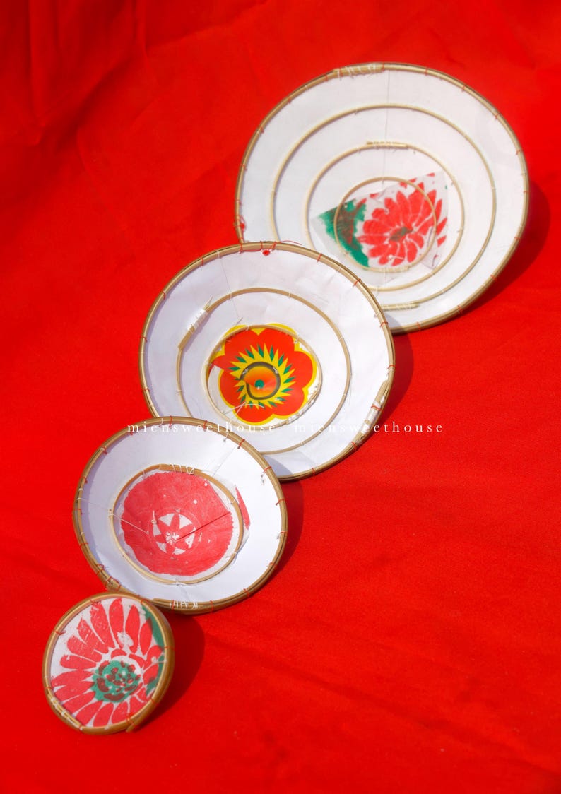 May include: Four white, circular decorative pieces with floral designs in red, green, and yellow, arranged on a red background. Each piece has a gold-colored rim and a spiral design. The sizes vary, with the largest at the top.