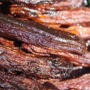 May include: Close-up of a pile of dark brown, shiny, dried banana slices. The banana slices are arranged in a random pattern and appear to be coated in a sweet glaze.