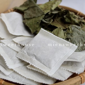 Puede incluir: Primer plano de una cesta tejida llena de bolsitas de té blancas y hojas verdes secas. El texto "miensweethouse" es visible en las bolsitas de té y las hojas.
