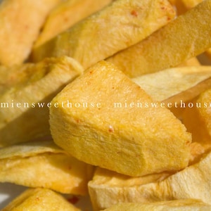 Op de afbeelding: Een close-up van een stapel goudbruine gebakken banaan chips. De chips zijn in een willekeurig patroon gerangschikt, met sommige overlappend.