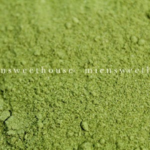 May include: Close-up of a bowl of green powder. The powder is finely ground and has a uniform texture. The powder is likely a type of matcha or other green tea powder.