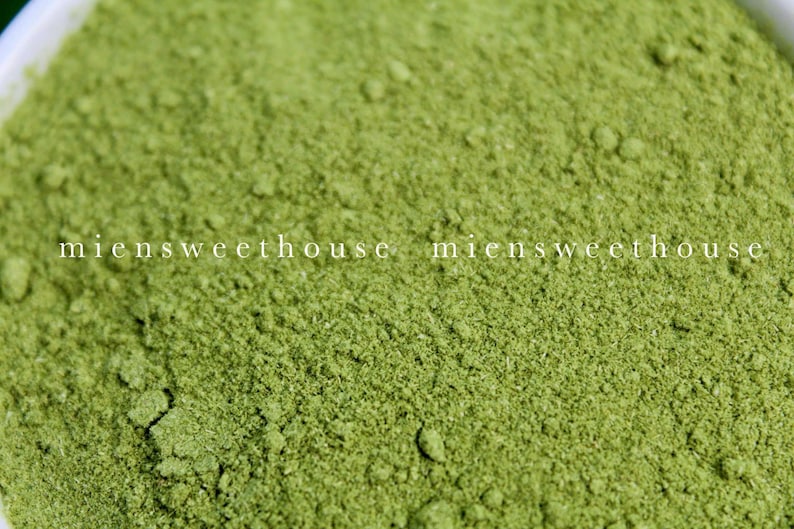 May include: Close-up of a bowl of green powder. The powder is finely ground and has a uniform texture. The powder is likely a type of matcha or other green tea powder.