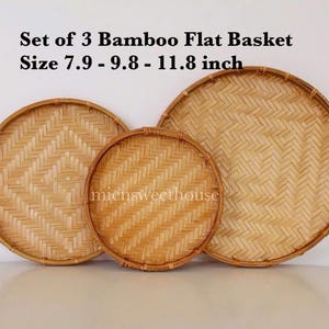 May include: Set of three woven bamboo flat baskets in different sizes. The baskets are round and have a natural brown color. The largest basket is 11.8 inches in diameter, the middle basket is 9.8 inches in diameter, and the smallest basket is 7.9 inches in diameter.