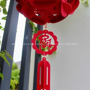 May include: Red felt Chinese New Year lantern with intricate cutouts and a tassel. The lantern has the Chinese character for "good fortune" hanging from it.
