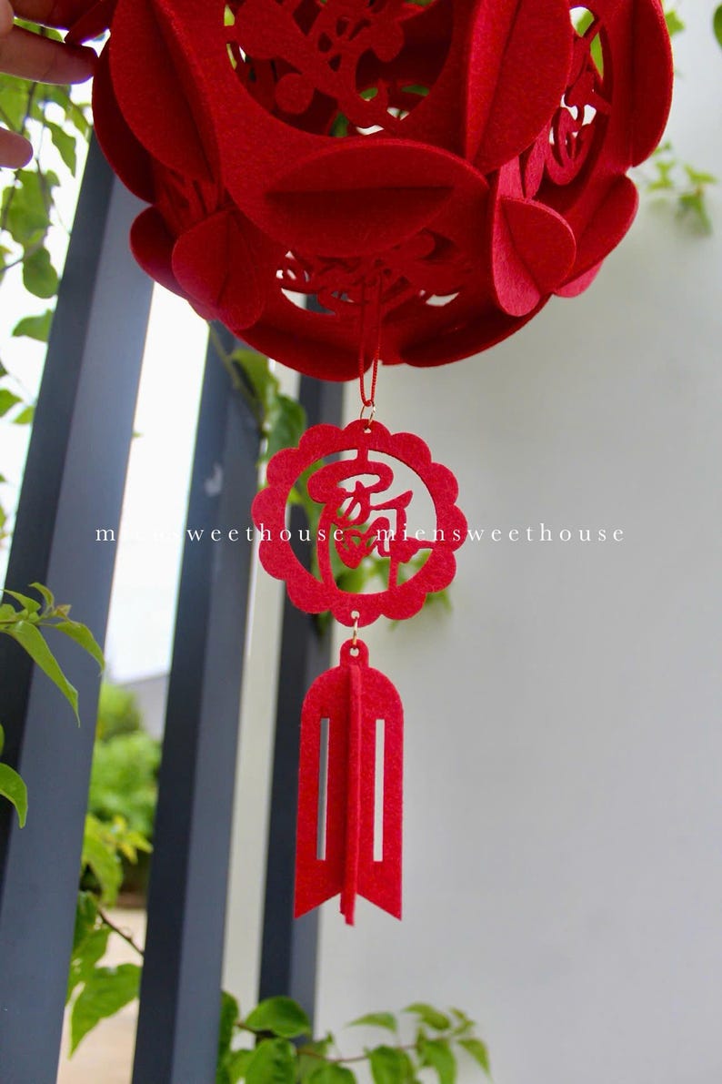 May include: Red felt Chinese New Year lantern with intricate cutouts and a tassel. The lantern has the Chinese character for "good fortune" hanging from it.