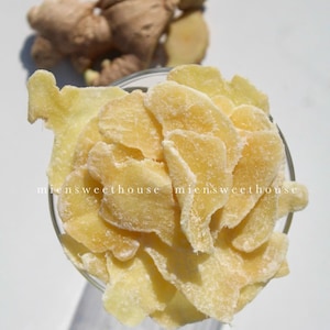 May include: A close-up of a bowl of candied ginger. The ginger is sliced thinly and coated in a white sugar glaze. The ginger is a light yellow color.