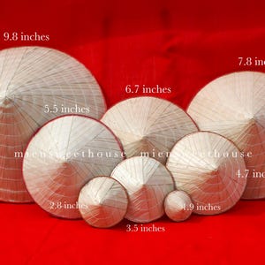 May include: A collection of conical straw hats of varying sizes, ranging from 1.9 inches to 9.8 inches in diameter, displayed against a red background. The hats are made of woven straw and have a traditional conical shape.