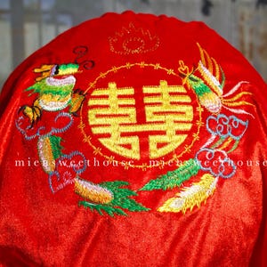 May include: Red fabric with gold embroidery featuring a double happiness symbol, a dragon, and a phoenix. The embroidery is in shades of green, yellow, and white. The text "micsweethouse" is visible.