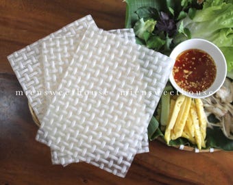 May include: Three white rice paper sheets with a woven pattern, a bowl of red dipping sauce, and a plate of yellow and green vegetables.