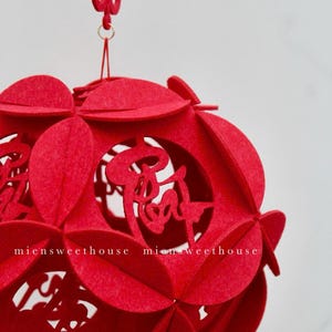 May include: Red felt Chinese lantern with intricate cutouts and a traditional knot at the top. The lantern is decorated with Chinese characters.