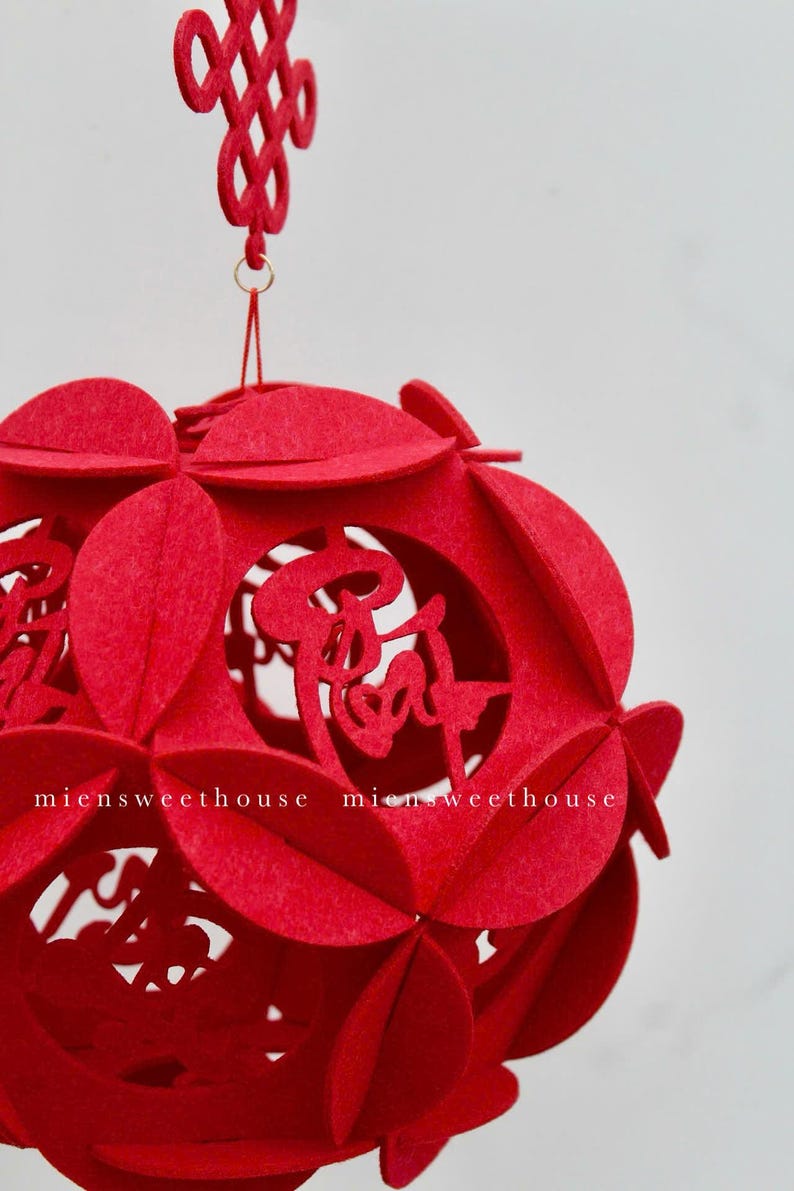 May include: Red felt Chinese lantern with intricate cutouts and a traditional knot at the top. The lantern is decorated with Chinese characters.