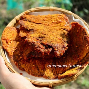 Pode incluir: Uma cesta redonda de vime contém vários pedaços de carne seca, com um tom avermelhado-alaranjado e especiarias visíveis. A carne está disposta sobre um forro de papel branco. O texto "miensweethouse" é visível.