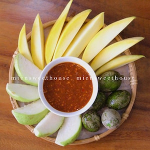 May include: A woven basket filled with sliced mango, guava, and green fruit. A small white bowl filled with a red sauce is in the center of the basket. The text "miensweethouse" is visible on the basket.
