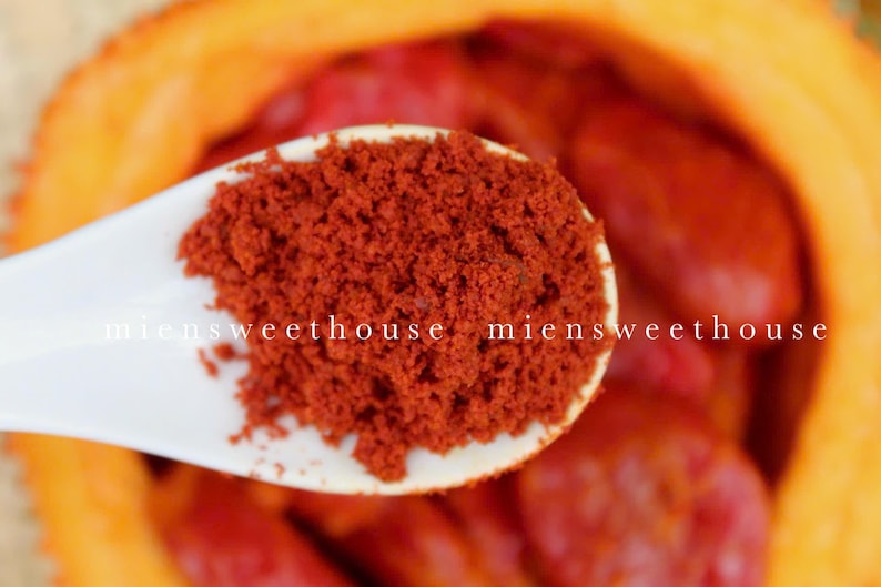 Pu&ograve; includere: Un cucchiaio di ceramica bianca pieno di polvere di paprika rosso vivo. Il cucchiaio &egrave; appoggiato su una ciotola di frutta rossa e arancione.