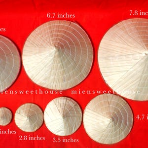 May include: A collection of conical straw hats in various sizes, ranging from 1.9 inches to 7.8 inches in diameter. The hats are arranged on a red background, showcasing their traditional design and craftsmanship. The hats are made of woven straw.