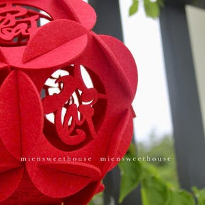 May include: A red felt Chinese lantern with intricate cutouts of Chinese characters. The lantern is hanging from a string and has a gold tassel.