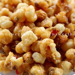 以下が含まれることがあります： 金色の艶出しされたトウモロコシの粒の山をクローズアップ。粒はわずかに不規則な形をしており、光沢のある質感で、赤色のヒントがいくつか見られます。「miensweethouse」というテキストが画像に表示されています。