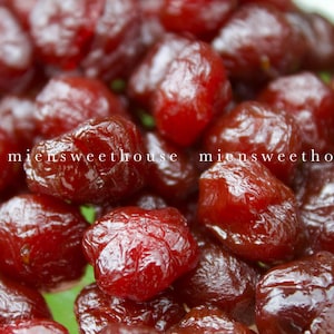 Puede incluir: Primer plano de un montón de frutos secos de color marrón rojizo brillante. La fruta parece regordeta y ligeramente translúcida, con un brillo brillante. El texto "miensweethouse" es visible en blanco. La imagen sugiere un aperitivo o ingrediente.