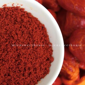 Pu&ograve; includere: Una ciotola bianca piena di polvere di paprika rosso vivo. La polvere &egrave; finemente macinata e ha una consistenza liscia. La ciotola &egrave; appoggiata su un frutto rosso e arancione.