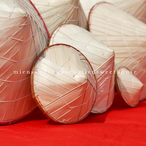 May include: A collection of woven straw hats in various shapes and sizes, arranged on a vibrant red surface. The hats are made of light-colored straw and feature a distinctive woven pattern. The image includes the text "miensweethouse".