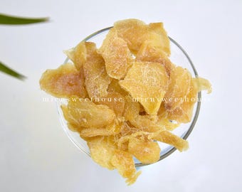 May include: A clear glass bowl filled with candied ginger slices. The ginger is a light golden color with a crystallized sugar coating. The image is taken from above, with the bowl centered on a white background. The text "micusweethouse" is visible.