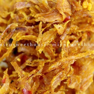 May include: Close-up of a pile of crispy, golden brown, shredded pork with red chilli flakes. The pork is arranged in a random pattern, creating a visually appealing texture.