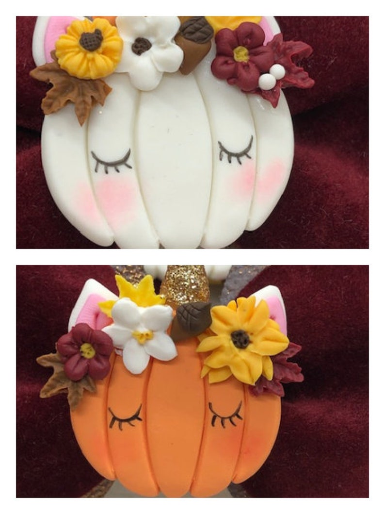 Pu&ograve; includere: Due ornamenti a forma di zucca con corna di unicorno, uno bianco e uno arancione, decorati con fiori e foglie autunnali.