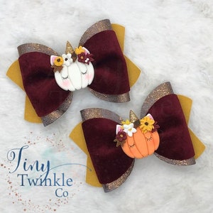 Pu&ograve; includere: Due fiocchi per capelli in velluto bordeaux con dettagli in glitter dorati. Ogni fiocco presenta una zucca in pasta polimerica fatta a mano con un corno di unicorno e dettagli floreali.