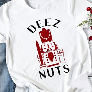 May include: White t-shirt featuring a red and white nutcracker illustration with the text "DEEZ NUTS" in black.