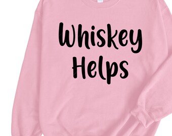 Könnte beinhalten: Hellrosa Sweatshirt mit dem Aufdruck "Whiskey Helps" in fetten, schwarzen Buchstaben. Das Sweatshirt hat einen Rundhalsausschnitt und lange Ärmel.