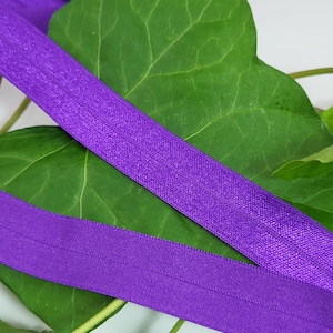 Könnte beinhalten: Lilafarbener elastischer Besatz mit schimmerndem Finish, gezeigt auf einem grünen Blatt Hintergrund.