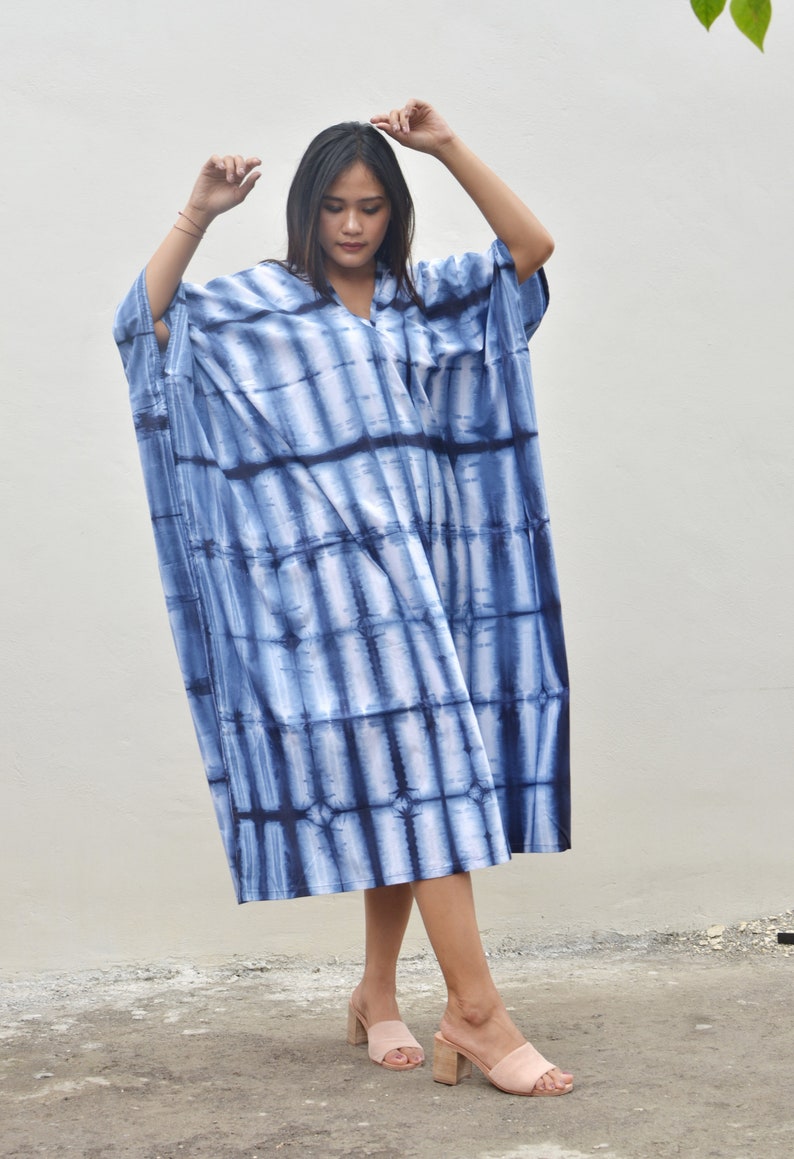 May include: A long, flowing blue and white tie-dye dress with a V-neckline. The dress is loose-fitting and has a relaxed silhouette.