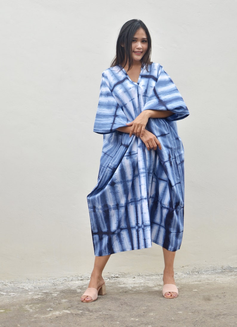 May include: A blue and white tie-dye maxi dress with a V-neck and 3/4 sleeves. The dress is loose-fitting and has a flowing silhouette.