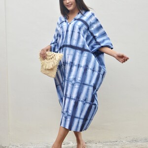 May include: A woman wearing a blue and white tie-dye maxi dress with a straw bag and beige sandals.