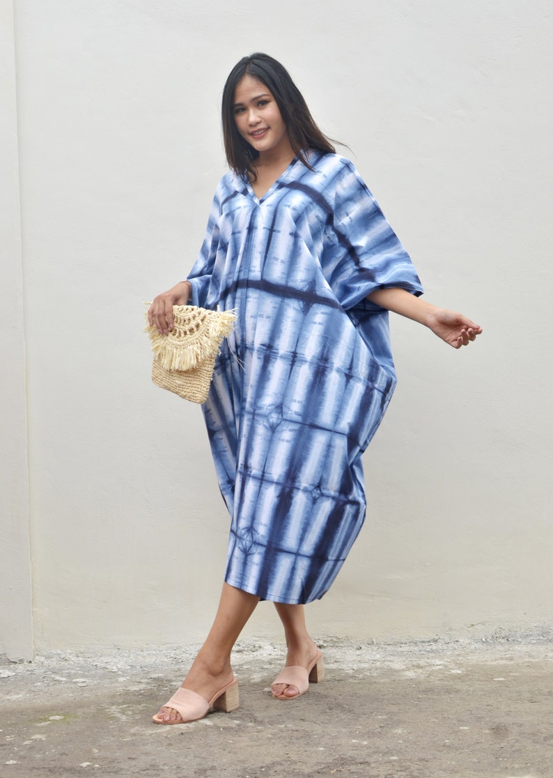 May include: A woman wearing a blue and white tie-dye maxi dress with a straw bag and beige sandals.