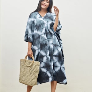 Puede incluir: Una mujer con un vestido maxi de tie-dye negro y blanco, un bolso de mano de paja y sandalias rosas.