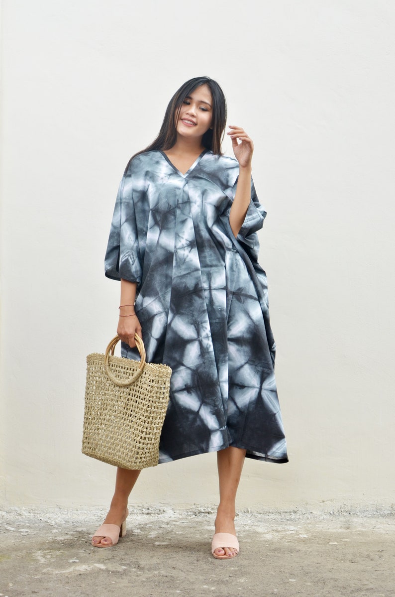 Puede incluir: Una mujer con un vestido maxi de tie-dye negro y blanco, un bolso de mano de paja y sandalias rosas.