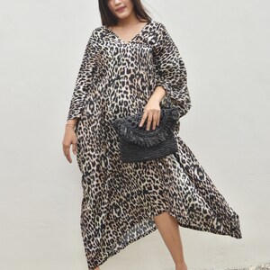 May include: A woman wearing a long, brown and black leopard print dress with a black woven clutch bag and pink sandals.