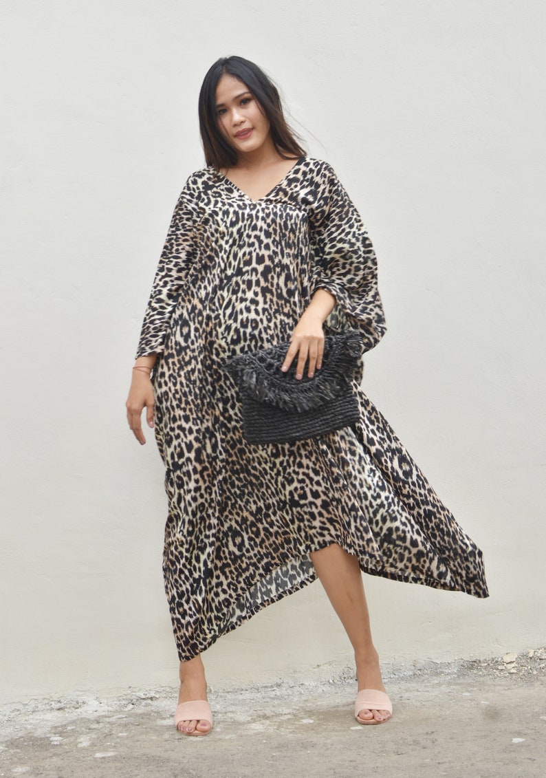 May include: A woman wearing a long, brown and black leopard print dress with a black woven clutch bag and pink sandals.